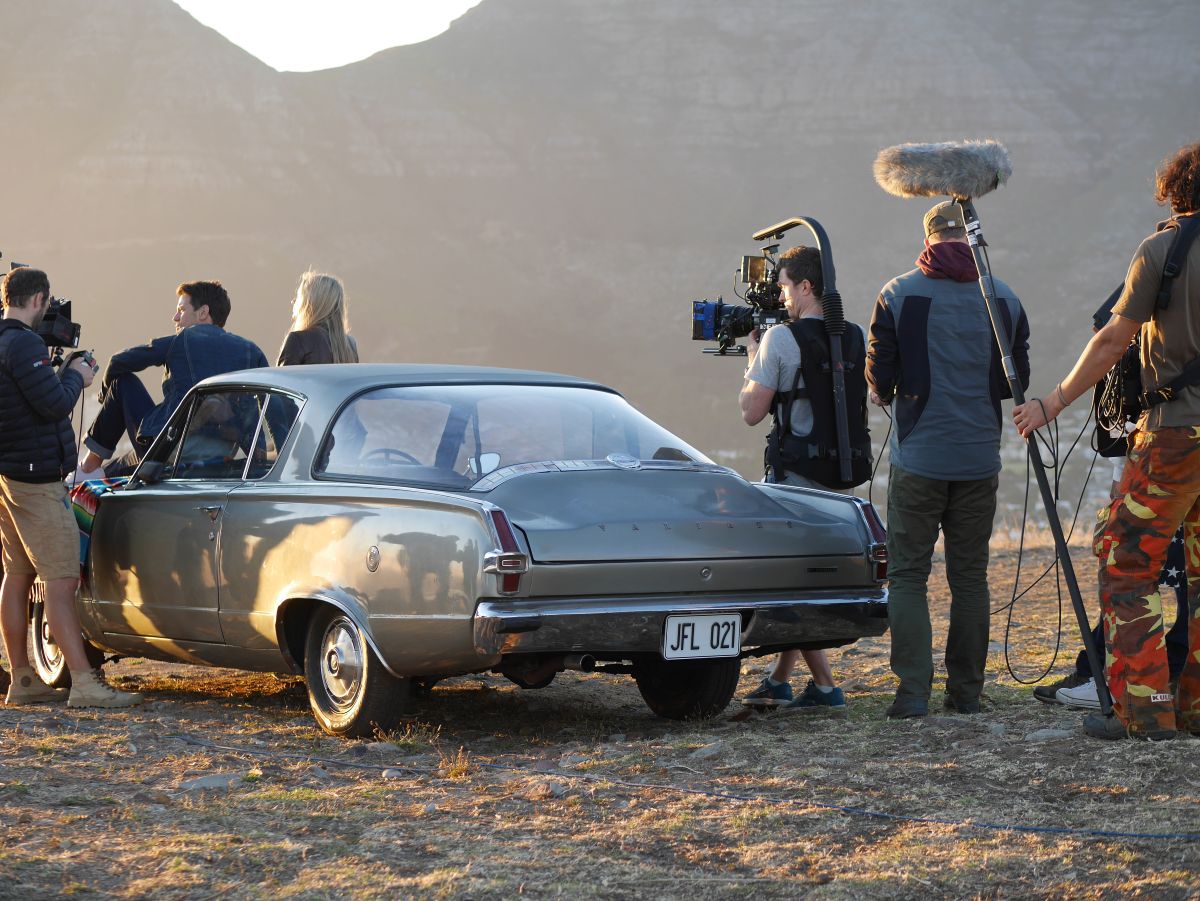 A couple sitting on a car being filmed